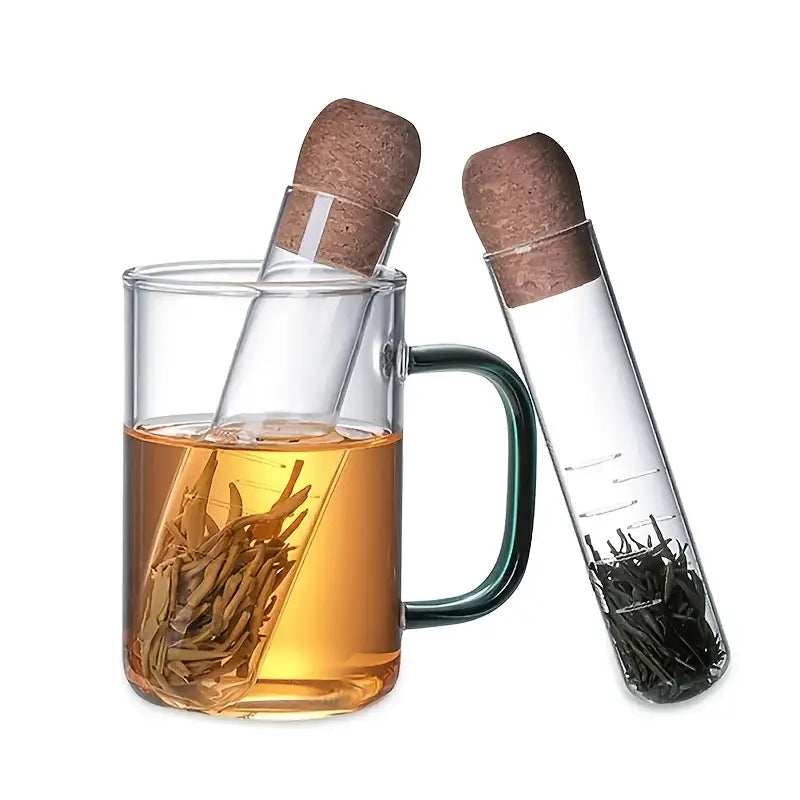 A glass tea infuser with a cork stopper, shown alongside a mug filled with tea and a separate tube filled with tea leaves.